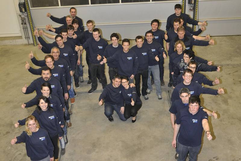 Gruppenfoto des Teams, 2013: Mitarbeitende in einer Halle, mit dem Daumen nach oben
