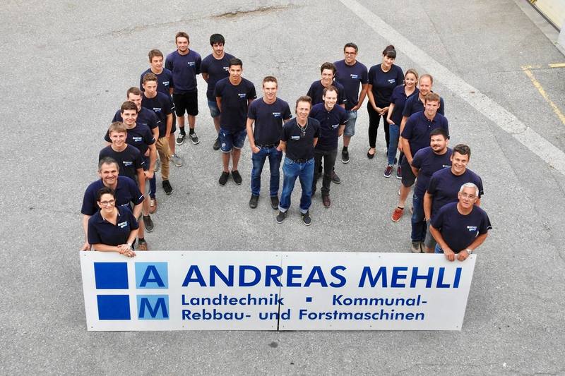 Gruppenfoto des Teams, 2022: Mitarbeitende in M-Formation über dem Firmenschild Andreas Mehli