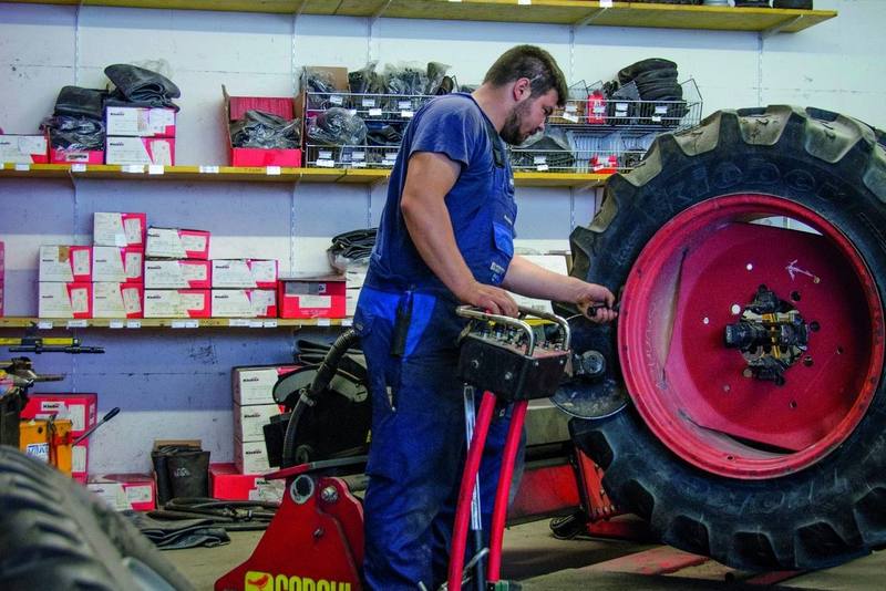 Mechaniker montiert einen Traktorreifen auf der Montiermaschine, im Regal dahinter Reifen und Schläuche